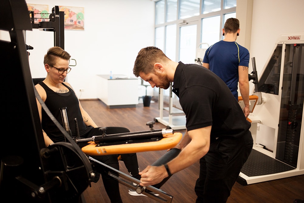 Physiotherapeut von Physics in Wasserburg am Inn unterstützt Patienten:innen am Traininginsgerät