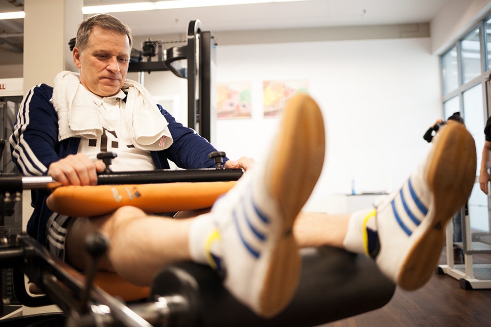 Ein Patient trainiert an einer Beinpresse, bei der er mit den Füßen nach unten drückt, um seine Oberschenkelmuskulatur zu stärken.