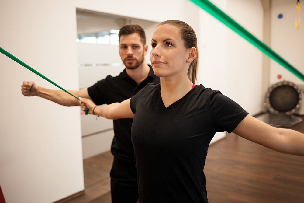 Physiotherapeut von Physics leitet eine Frau beim Training mit TRX-Bändern an.