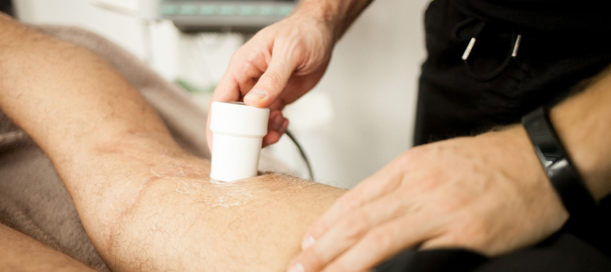 Bild auf dem ein Physiotherapeut mit einem Ultraschallgerät den hinteren Obershenkel eines liegenden Patienten untersucht