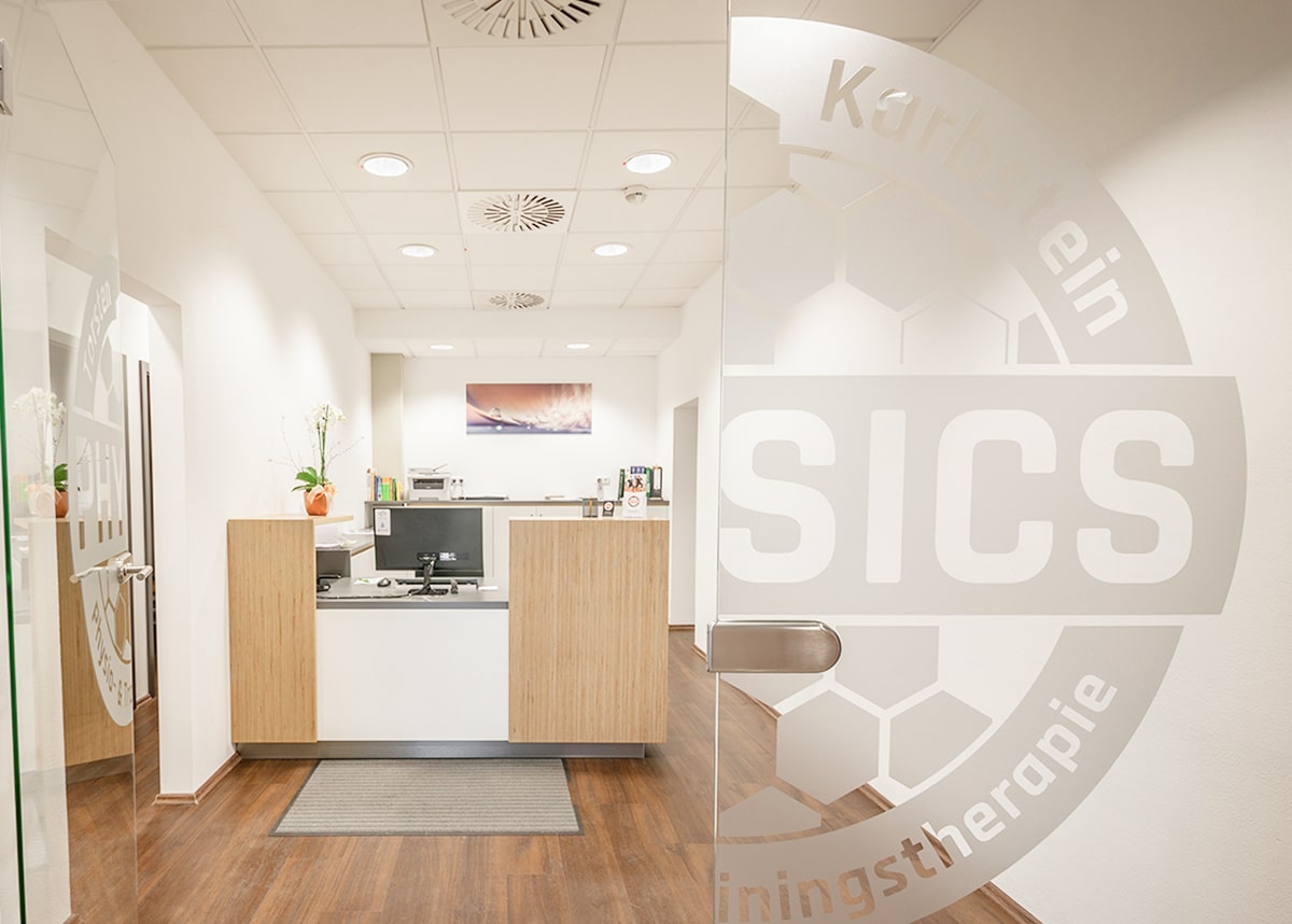 Eingangsbereich mit halb geöffneter Glastür zur Rezeption der Physiotherapie PHYSICS, mit Praxislogo auf der Tür.